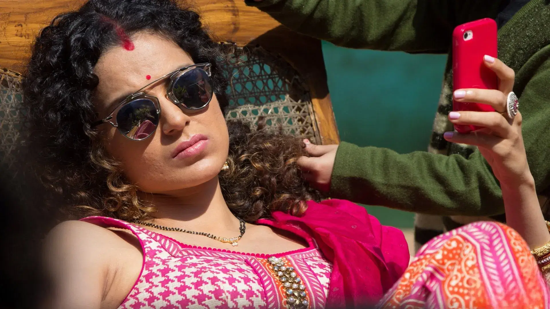 Σκηνή από την ταινία «Tanu Weds Manu: Returns» (2015) με γυναίκα σε παραδοσιακή ενδυμασία να κρατά κόκκινο κινητό και να ξαπλώνει σε ψάθινη καρέκλα.