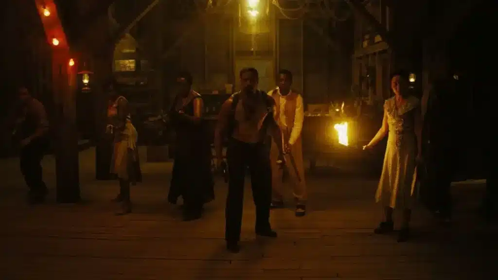 Σκηνή από το Sinners (2025), ομάδα ανθρώπων οπλισμένων με όπλα και δάδα στέκεται σε σκοτεινή ξύλινη αποθήκη έτοιμη για τελετουργική σύγκρουση.