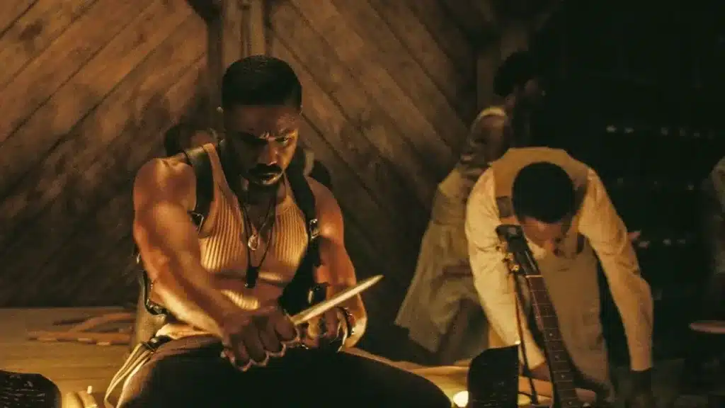 Σκηνή από το Sinners (2025), μυώδης άντρας κρατά μαχαίρι σε τελετουργικό δωμάτιο με κεριά, ενώ στο βάθος άλλοι συμμετέχουν στο σκοτεινό δρώμενο.