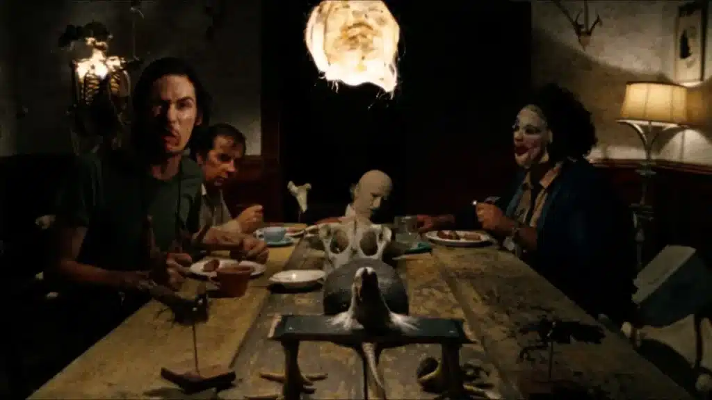 Δείπνο τρόμου στο μισοσκόταδο, άντρες κάθονται γύρω από παλιό ξύλινο τραπέζι, διακοσμημένο με κόκαλα και ταριχευμένα ζώα, μέσα στο μακάβριο σπίτι της οικογένειας στο The Texas Chain Saw Massacre (1974).